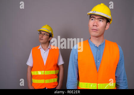 Deux jeunes hommes asiatiques construction worker ensemble contre ba gris Banque D'Images