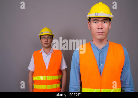 Deux jeunes hommes asiatiques construction worker ensemble contre ba gris Banque D'Images