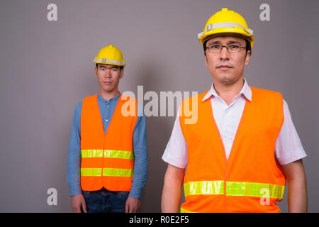 Deux jeunes hommes asiatiques construction worker ensemble contre ba gris Banque D'Images