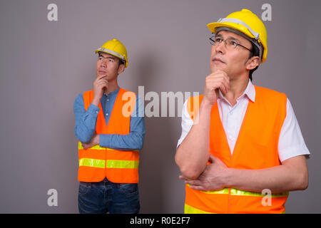 Deux jeunes hommes asiatiques construction worker ensemble contre ba gris Banque D'Images