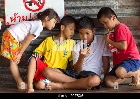 SANGHLABURI, Thaïlande, le 24 janvier 2016 : un groupe d'enfants thaïlandais est à regarder ou jouer sur un smartphone, sous le hall de la passerelle dans Sanghlaburi, Mon Banque D'Images