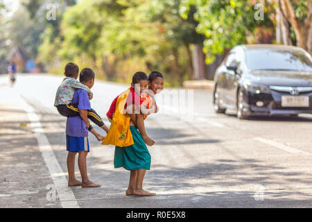 SANGHLABURI, Thaïlande, le 24 janvier 2016 : Les enfants sont petits frères sur le dos pour traverser la route à Sangkhlaburi, Thaïlande Banque D'Images