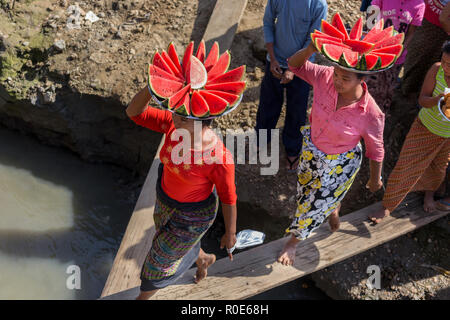 MANDALAY, Myanmar, le 21 janvier 2015 : les birmanes sont à bord d'un bateau en marche sur une planche en bois, transportant des tranches de pastèque sur la tête en ma Banque D'Images