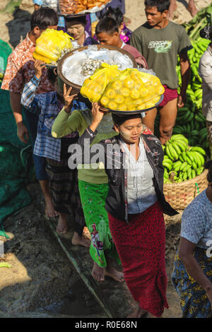 MANDALAY, Myanmar, le 21 janvier 2015 : les birmanes sont à bord d'un bateau en marche sur une planche en bois, transportant des légumes sur leurs têtes à Mandalay, Banque D'Images