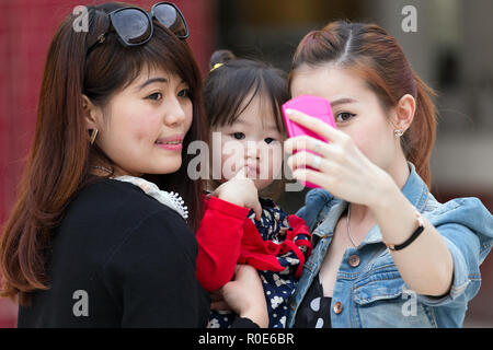 MANDALAY, Myanmar, le 16 janvier 2015 : les femmes coréennes sont le tournage d'un autoportrait (selfies) avec une drôle de petite fille s'ennuie dans une rue de Mandalay, Myanmar Banque D'Images