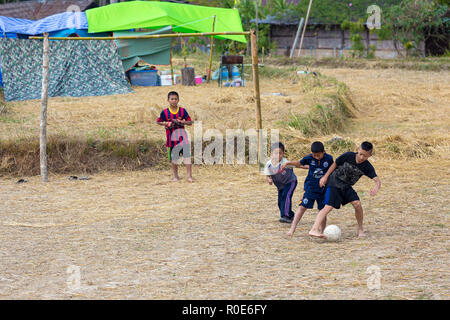 MAE KLANG LUANG, Thaïlande, le 31 décembre 2014 : Quelques enfants jouent au soccer football dans un champ de riz récolté à sec dans le village de Mae Klang Luang, Banque D'Images