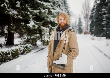 Thème Sports d'hiver. Portrait. Beau jeune homme de race blanche avec de longs cheveux et barbe rouge. En hiver pose modèle snow park contre l'arrière-plan de la fo Banque D'Images
