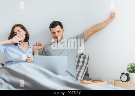 Famille passer du temps ensemble dans la chambre, s'étirer et bailler comme se lever tôt, faire le travail à distance sur ordinateur portable, utilisez une connexion wifi, de boire du café, être Banque D'Images