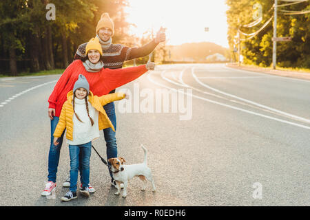 Portrait d'une jolie femme, son mari et sa fille afficher ok sign, promenade avec chien sur route, profiter du soleil, ont une vie active. Friendly family Banque D'Images