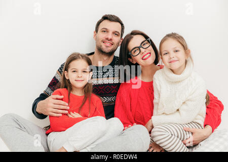 Portrait de famille : mère, père et deux sœurs regarder directement dans la caméra, les expressions positives, s'embrassent et sourire joyeusement, isolé Banque D'Images