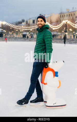 Portrait d'homme barbu joyeux se trouve près de skate, de l'aide allant à patiner pour première fois, d'être dans la bonne humeur, bénéficie d'vacances d'hiver. Heureux l'homme non rasé Banque D'Images