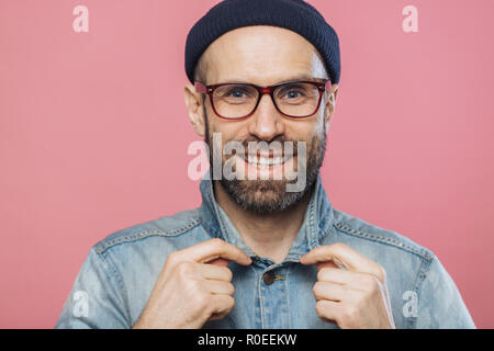 De l'horizontale à barbu souriant agréable homme porte des lunettes et veste en jean, nouveau advertizes des vêtements à la mode, heureuse expression a, iso Banque D'Images