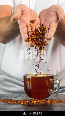 L'homme à la table verse de l'altitude d'un mélange de fruits et d'herbes dans un verre de thé rouge Banque D'Images