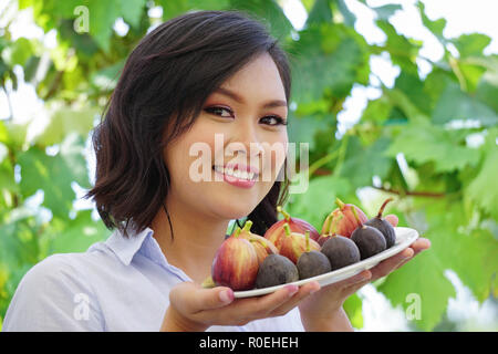 Belle jeune femme asiatique sourire tout en maintenant une assiette de fruits frais fig. Un bon concept photo pour la promotion de la santé de manger des fruits les aliments et l'alimentation Banque D'Images