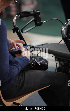 Une vieille femme s'appuyant sur son smartphone avec un doigt. Un senior lady assis sur la chaise et sa3903 est très proche. Un sac à main noir. Banque D'Images