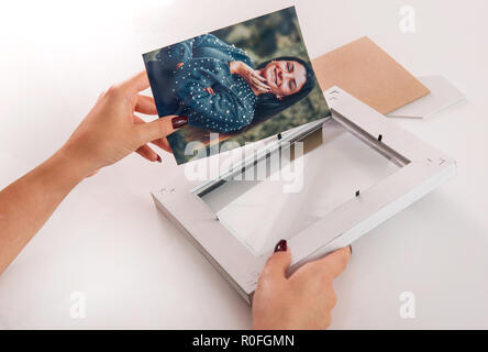 Femme de placer une photo couleur d'une dame souriante dans un simple cadre en bois blanc dans une vue en gros plan de ses mains Banque D'Images