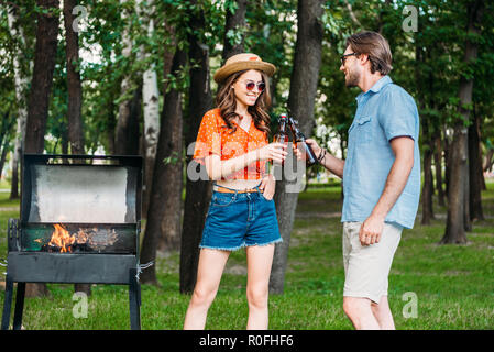 Jeune couple à lunettes de cliquetis de bouteilles de bière au cours d'un barbecue dans le parc Banque D'Images