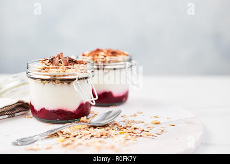 Petit déjeuner sain. Deux pots de yogourt saine avec sauce aux fraises, l'avoine et le chocolat sur une assiette de marbre blanc sur fond bleu avec l'exemplaire sp Banque D'Images