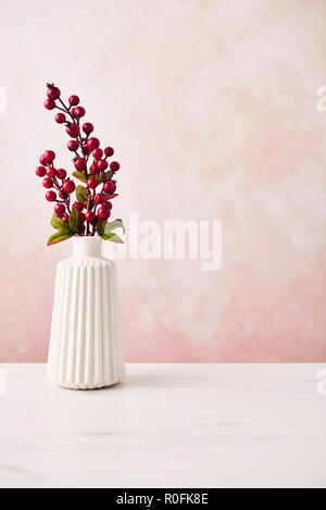 Décoration artificiel intérieur. Twig avec baies dans le vase sur la table en marbre blanc sur fond de mur rose. Copier l'espace. Banque D'Images