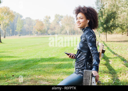 Femme de remise en forme avec plaisir à écouter la musique après l'entraînement au parc, s'appuyant sur clôture en bois dans la nature, à la recherche de distance et prêt pour continuer Runni Banque D'Images