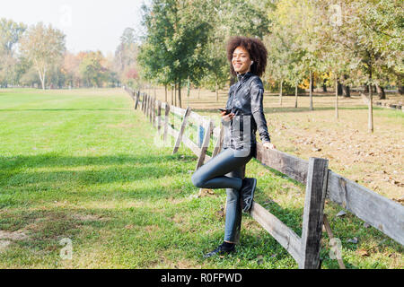 Femme de remise en forme avec plaisir à écouter la musique après l'entraînement au parc, s'appuyant sur clôture en bois dans la nature, à la recherche de distance et prêt pour continuer Runni Banque D'Images