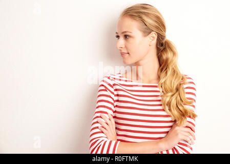Portrait de la belle jeune femme portant chemise rayée en se tenant debout à l'arrière-plan blanc isolé. Banque D'Images