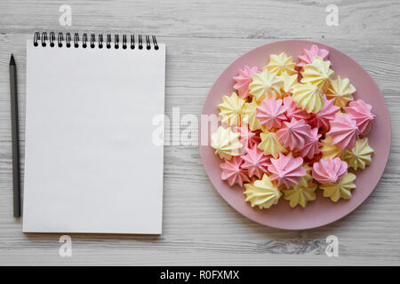 Mini meringues sur la plaque rose et blank notepad sur un fond en bois blanc, vue du dessus. Close-up. L'espace pour le texte. Banque D'Images