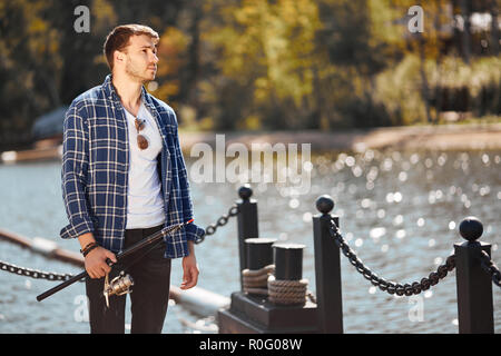 Jeune pêcheur avec rod et lunettes de la pêche dans le lac Banque D'Images