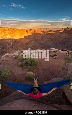 Randonneur repose sur un hamac en admirant le coucher du soleil de la branche est du Shafer Canyon près de Dead Horse Point State Park Canyonlands Utah Banque D'Images