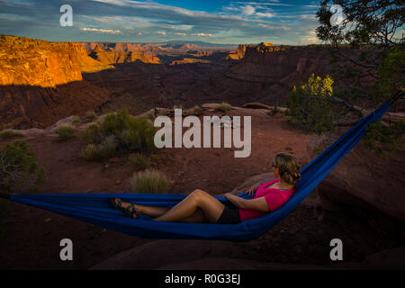 Randonneur repose sur un hamac en admirant le coucher du soleil de la branche est du Shafer Canyon près de Dead Horse Point State Park Canyonlands Utah Banque D'Images