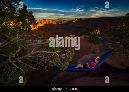 Randonneur repose sur un hamac en admirant le coucher du soleil de la branche est du Shafer Canyon près de Dead Horse Point State Park Canyonlands Utah Banque D'Images