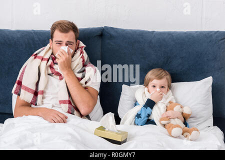 Père et fils malade nez de soufflage avec serviettes en papier en position couchée au lit et looking at camera Banque D'Images