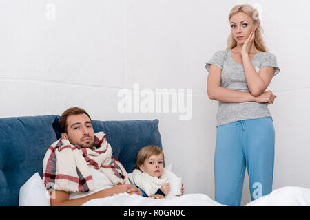 Femme debout près de confondre mari malade et son fils et à la caméra en tant qu'ils au lit Banque D'Images