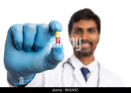 Pilule rouge et jaune présenté par Indian male medic portant des gants en latex bleu isolé sur fond blanc Banque D'Images