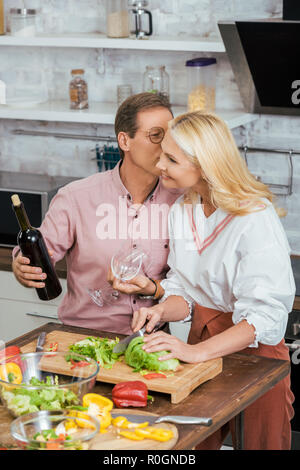 Mari et femme s'embrasser tenant une bouteille de vin pendant le dîner à la maison Banque D'Images