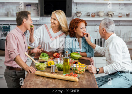 Heureux les couples d'âge mûr se nourrir les uns les autres au cours de la préparation de la salade pour le dîner à la maison Banque D'Images