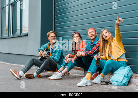 Les gens branchés de passer du temps ensemble sur la rue tandis que l'homme jouant de la guitare acoustique et de la girl pointing Banque D'Images