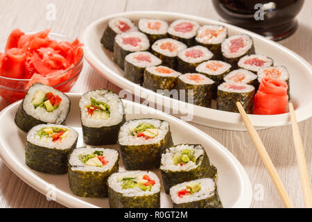 Différents rouleaux de sushi avec du riz et des feuilles d'algues sur une plaque en céramique, le flacon en verre avec de la sauce soja et de gingembre mariné dans un bol Banque D'Images