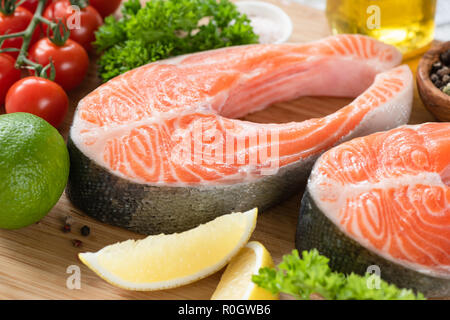 Darnes de saumon frais et d'ingrédients pour la cuisine, de l'huile d'olive épices tomates cerises et des feuilles de salade verte Banque D'Images