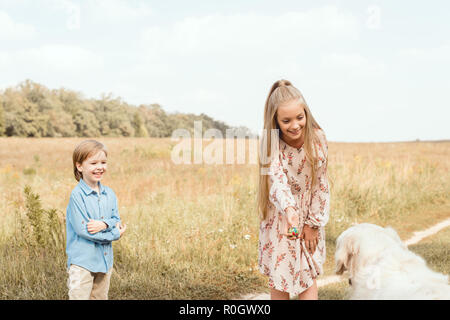 Adorables petits enfants jouer avec golden retriever dog in field Banque D'Images