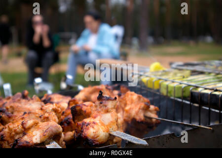 Avec des brochettes de viande de poulet rôti sur le grill chaud libre avec deux silhouettes humaines floues en arrière-plan Banque D'Images