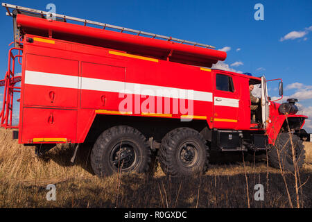 Location de camion rouge à travers l'Oural avec champ d'automne et de l'herbe jaune pâle contre le ciel bleu et les nuages. Le concept de forêt d'extinction Banque D'Images