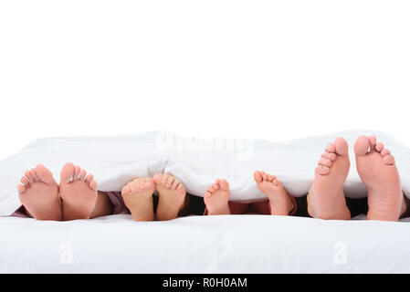 Pieds de la famille au lit sous couverture blanche, isolated on white Banque D'Images