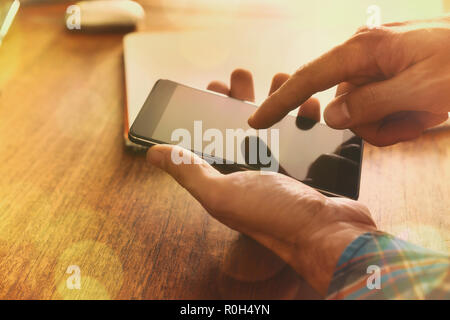 Les mains d'un homme touchant un téléphone sur une table en bois brun avec golden sunbeam. Composition horizontale. Banque D'Images