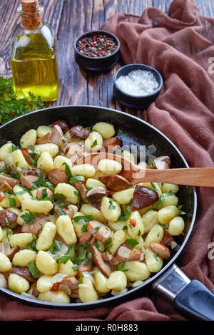 Gnocchi de pommes de terre aux cèpes sur une poêle avec une cuillère de bois sur une table en bois rustique avec un tissu marron, les épices et le persil au fond du Rhône, Banque D'Images