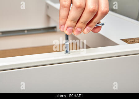 L'homme serre la cheville de cames en acier dans le cadre de la table faite de panneaux de particules avec une clé hexagonale, Flat pack assemblage de meubles. Banque D'Images