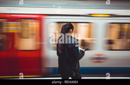 Londres - le 31 octobre 2018 : young woman reading magazine que l'excès de train de tube arrive sur la plate-forme du métro de Londres Banque D'Images