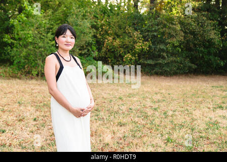 Belle pregnant asian woman standing in park outdoor Banque D'Images