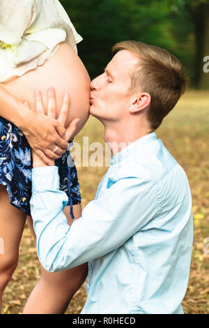 Jeune homme embrassant le ventre de femme enceinte outdoor Banque D'Images