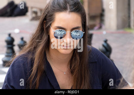 Une jeune femme jouant aux échecs avec la réflexion du conseil d'échecs dans ses lunettes de soleil. à Tel Aviv, Israël dans le marché Carmel. Banque D'Images